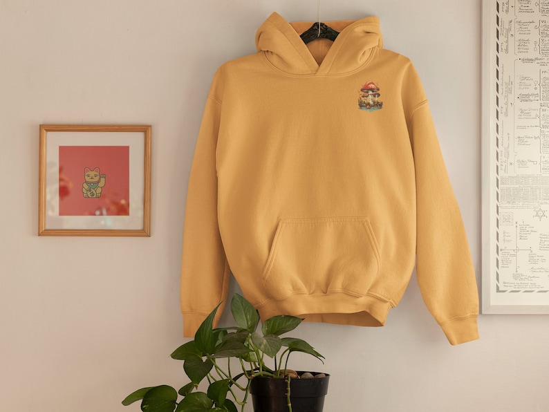 May include: A mustard yellow hoodie with a mushroom graphic on the left chest. The hoodie has a kangaroo pocket and a drawstring hood.