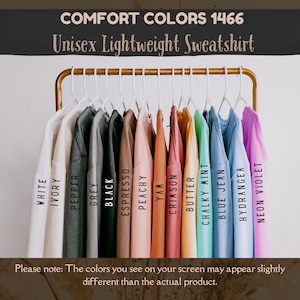 May include: A display of unisex lightweight sweatshirts in various colors, including white, black, and blue jean, hanging on a gold rack. The text "COMFORT COLORS 1466" and "Unisex Lightweight Sweatshirt" are visible.