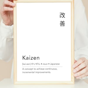 Puede incluir: Una impresión enmarcada con la palabra japonesa "改善" (kaizen) y la definición de la palabra en inglés. La definición dice: "[kai-zen] かいぜん  • sustantivo • japonés Un concepto para lograr mejoras continuas e incrementales."