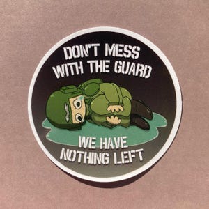 Può includere: Un adesivo rotondo con un'illustrazione a cartoni animati di un soldato in uniforme verde, sdraiato e che piange. L'adesivo ha il testo "DON'T MESS WITH THE GUARD" e "WE HAVE NOTHING LEFT" in bianco su sfondo nero.