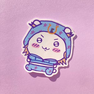 May include: A sticker featuring a cartoon character with a light blue outfit and hat, adorned with purple stars. The character has a white face with pink cheeks, a small mouth, and expressive eyes. The sticker has a white border and is set against a light purple background.