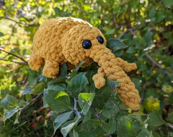 Op de afbeelding: Een gehaakt pluche speelgoed in de vorm van een insect met een lange snuit en grote ogen. Het speelgoed is lichtbruin van kleur en zit op een tak van een boom.