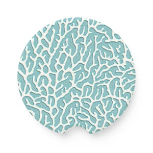 May include: A circular car coaster featuring a turquoise backdrop and a white coral reef design. The coaster has a small notch for easy removal. The pattern is a repeating coral design. The coaster is designed to fit in a car cup holder.