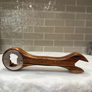 Peut inclure: Un ouvre-bouteille en bois en forme de clé à molette avec un ouvre-bouteille en métal argenté. La clé à molette est en bois foncé avec un motif rayé.