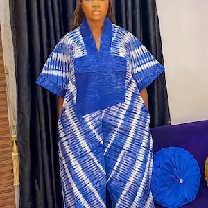May include: A floor-length kaftan featuring a vibrant blue and white tie-dye pattern with diagonal stripes. The garment has short, wide sleeves, a solid blue rectangular chest panel, and a V-neckline, creating a loose and flowing silhouette.