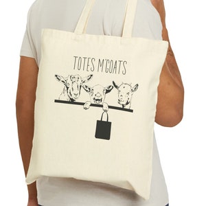 May include: A person is carrying a beige tote bag with a black graphic of three goats peeking over a ledge. The text "Totes McGoats" is printed on the bag.