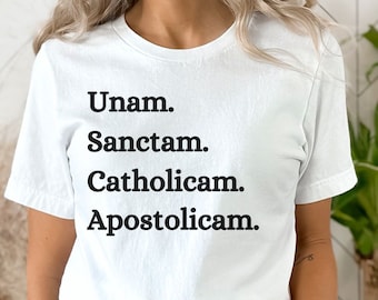 Peut inclure: T-shirt blanc avec du texte noir qui dit "Unam. Sanctam. Catholicam. Apostolicam."