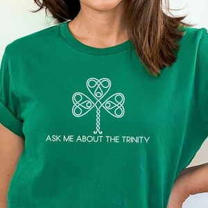 May include: A green t-shirt with a white shamrock design and the text "Ask Me About The Trinity".