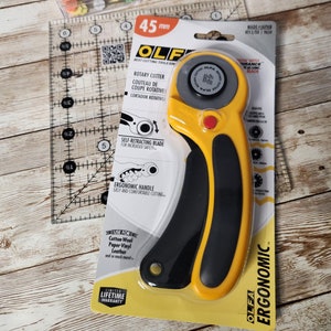May include: Yellow and black rotary cutter with a self-retracting blade. The cutter is 45 mm and has an ergonomic handle. The packaging says "Olfa Ergonomic" and "Best Cutting Tools Since 1956".