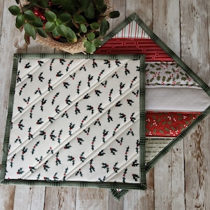 May include: Two quilted pot holders, one with a green and white holly leaf pattern and the other with a multi-colored patchwork design. The patchwork design includes red, white, and green fabrics.