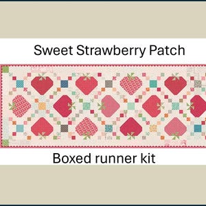 May include: A rectangular quilt runner kit with a strawberry pattern. The design features alternating red and pink strawberries with green stems, set against a light background. The text "Sweet Strawberry Patch" and "Boxed runner kit" are displayed.