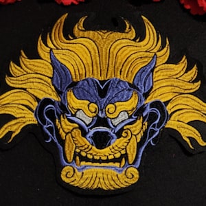 Peut inclure: Patch brodé représentant une représentation stylisée et détaillée d'un masque de démon japonais. Le masque est bleu et violet avec des accents dorés et une expression féroce. Le masque est entouré d'une crinière de cheveux jaunes.