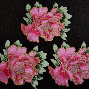 May include: Three pink and green embroidered fabric flower patches. The flowers are in a peony style with a pink and gold outline.