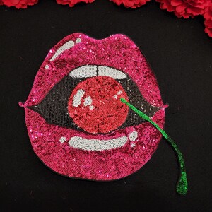 May include: A pink sequined lips patch with a red cherry and green stem. The cherry is also covered in sequins.