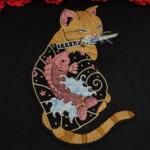 May include: Embroidered patch featuring a ginger cat holding a katana in its mouth. The cat has a koi fish design on its body, with pink, blue, and black accents. The patch is likely for clothing or accessories.