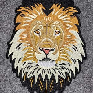 May include: Embroidered lion patch featuring a detailed design with a black mane, golden and white fur, and a pink nose. The patch is likely for clothing or accessories, adding a decorative element.