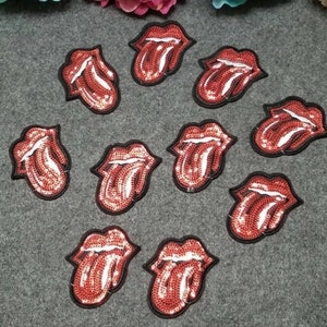 May include: Ten red and white sequined tongue patches with black outlines. The patches are arranged in a circle on a gray surface.