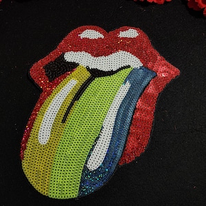May include: A colorful sequined patch of a red mouth with a rainbow tongue sticking out. The tongue is green, yellow, white, blue, and iridescent.