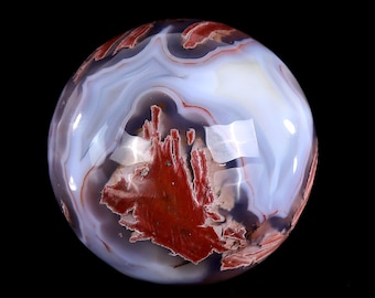 May include: A polished agate sphere with a swirling pattern of white, red, and brown. The sphere is smooth and translucent, with a high gloss finish.