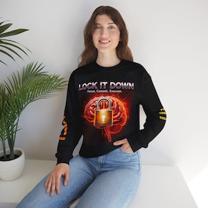 May include: Black sweatshirt featuring the text "LOCK IT DOWN" above a brain graphic with a padlock. The graphic is in shades of red, orange, and gold. The sleeves have additional text in orange.