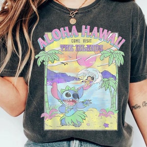 May include: Black t-shirt with a graphic print of Stitch from Lilo & Stitch. The graphic features Stitch in a hula skirt with a sunset and palm trees in the background. The text "Aloha Hawaii Come Visit The Islands" is printed above the graphic.