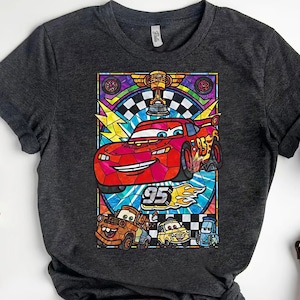 May include: Dark gray t-shirt featuring a colorful graphic of Lightning McQueen from the movie Cars. The design includes the number 95, a checkered flag, and other characters. The graphic is in a stained glass style.