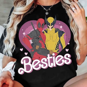 May include: Black t-shirt with a pink heart graphic featuring Deadpool and Wolverine. The text "Besties" is written in pink letters below the graphic.