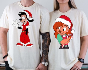 May include: A pair of white t-shirts with a Christmas theme. One shirt features Goofy dressed as Santa Claus, while the other shirt features a cartoon dog wearing a Santa hat and holding a candy cane.
