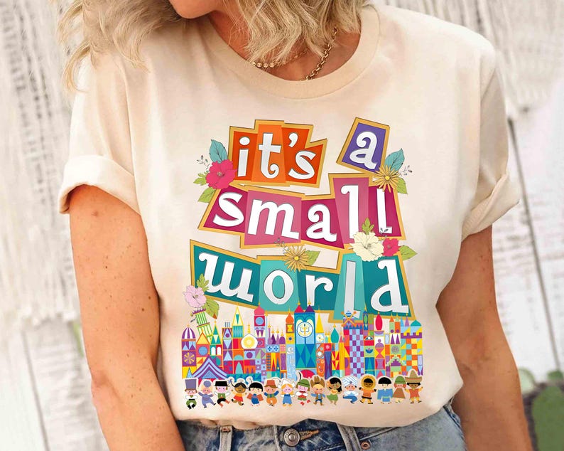 Puede incluir: Una camiseta blanca con el texto "it's a small world" en letras de colores y un gr&aacute;fico del paseo "it's a small world" en Disney World.