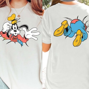 Könnte beinhalten: Weißes T-Shirt mit einer Cartoon-Grafik von Goofy, der vorne und hinten durch eine Wand bricht. Die Grafik auf der Vorderseite zeigt Goofy in einer roten Jacke, blauer Krawatte und gelbem Hut. Die Grafik auf der Rückseite zeigt Goofys Beine und gelbe Schuhe.