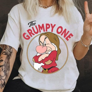 Op de afbeelding: Wit T-shirt met een rode en zwarte cartoon afbeelding van Grumpy uit Sneeuwwitje en de Zeven Dwergen. De tekst "The Grumpy One" is in rood op het shirt gedrukt.