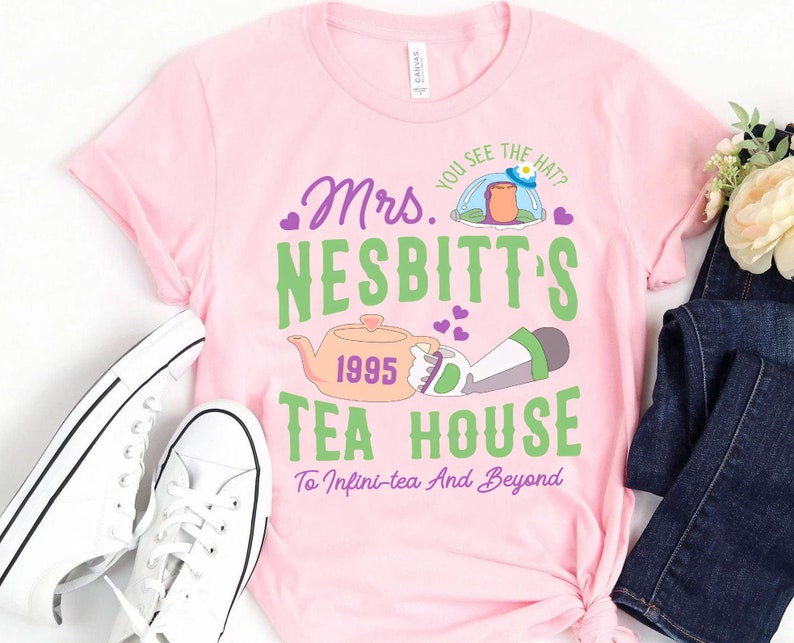 K&ouml;nnte beinhalten: Pinkes T-Shirt mit einem gr&uuml;nen und violetten Grafikdesign mit einer Teekanne, einer Comicfigur und dem Text "Mrs. Nesbitt's Tea House 1995 To Infini-tea And Beyond".