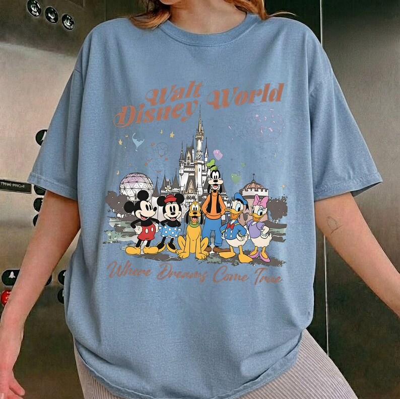 May include: Light blue t-shirt featuring a graphic of Disney characters including Mickey Mouse, Minnie Mouse, Goofy, Pluto, Donald Duck, and Daisy Duck. The shirt has the text "Walt Disney World" and "Where Dreams Come True".