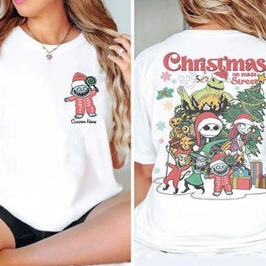 Puede incluir: Camiseta blanca con un gr&aacute;fico navide&ntilde;o en la espalda. El gr&aacute;fico presenta personajes de la pel&iacute;cula Pesadilla antes de Navidad, incluyendo a Jack Skellington, Sally y Oogie Boogie. El texto en la camiseta dice "Christmas on Main Street".