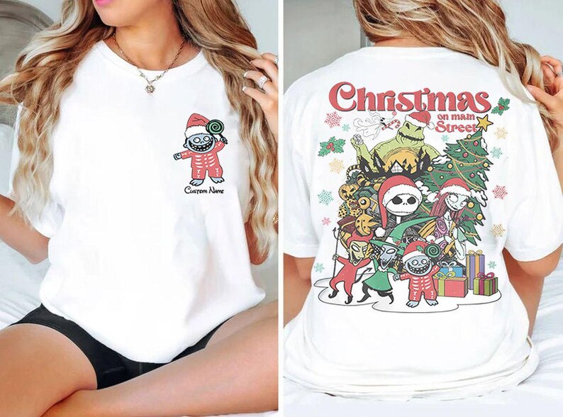 Puede incluir: Camiseta blanca con un gr&aacute;fico navide&ntilde;o en la espalda. El gr&aacute;fico presenta personajes de la pel&iacute;cula Pesadilla antes de Navidad, incluyendo a Jack Skellington, Sally y Oogie Boogie. El texto en la camiseta dice "Christmas on Main Street".
