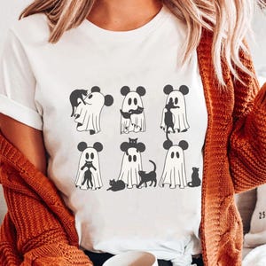 May include: White t-shirt featuring a design of black cats and ghosts wearing Mickey Mouse ears. The ghosts are holding the cats.