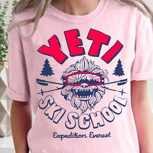 Puede incluir: Camiseta rosa con un gr&aacute;fico de un Yeti con gafas y el texto "YETI SKI SCHOOL Expedition Everest".
