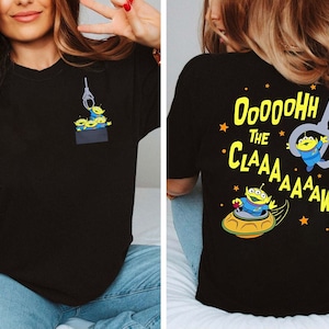 Puede incluir: Camiseta negra con un gráfico de tres extraterrestres verdes en la parte delantera y el texto "Dooooohh The Claaaaaaaaaw!" en la parte posterior.