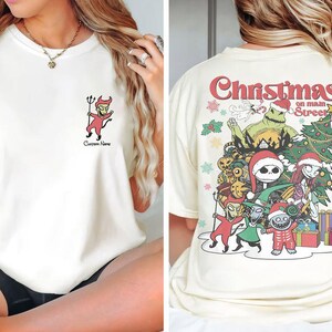 Puede incluir: Una camiseta blanca con un gr&aacute;fico de Navidad en la calle principal con personajes de Pesadilla antes de Navidad. El gr&aacute;fico incluye a Jack Skellington, Sally, Oogie Boogie y otros personajes.