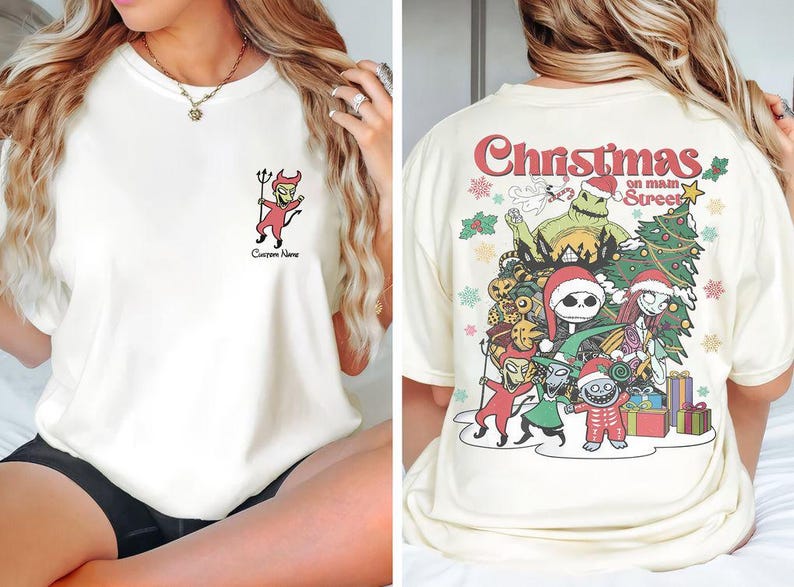 Puede incluir: Una camiseta blanca con un gr&aacute;fico de Navidad en la calle principal con personajes de Pesadilla antes de Navidad. El gr&aacute;fico incluye a Jack Skellington, Sally, Oogie Boogie y otros personajes.