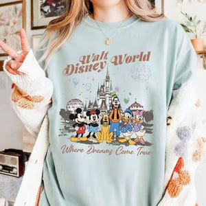 May include: A light blue sweatshirt featuring the text "Walt Disney World" above a graphic of Disney characters and Cinderella's castle. The phrase "Where Dreams Come True" is printed below the graphic.