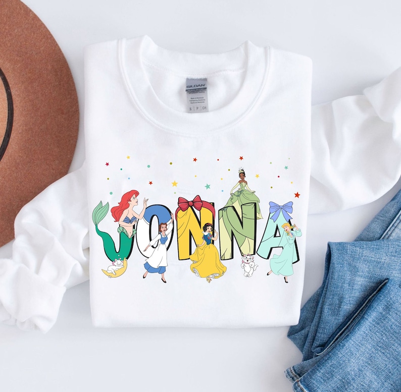 May include: White sweatshirt with a colourful design featuring Disney princesses spelling out the name "JONNA".