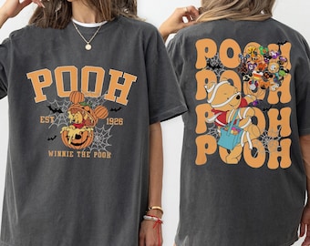 May include: Dark gray t-shirt featuring a Halloween-themed Winnie the Pooh design. The front displays "POOH" in orange block letters, with a pumpkin-themed Pooh Bear and the text "EST 1926". The back shows Pooh as a mummy and other characters in costumes.