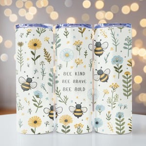 May include: Three white stainless steel tumblers with a floral pattern and bees. The middle tumbler has the text "Bee Kind Bee Brave Bee Bold" printed on it.