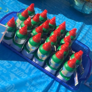 May include: A tray of green and red rocket-shaped party favours with a white and blue design. The favours are arranged in rows on a blue tray.