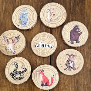 May include: A set of eight circular wood slices featuring illustrations of characters from The Gruffalo, including a blue monster, a mouse, an owl, a snake, a fox, and a brown monster, with one slice displaying the text The Gruffalo in black.