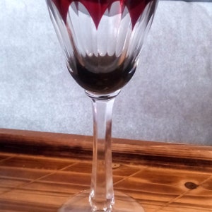 Könnte beinhalten: Ein hohes, klares Glas mit rotem Rand und einem geschliffenen Glasdesign. Das Glas hat einen langen Stiel und einen breiten Boden.