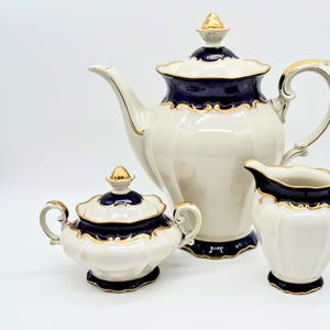 May include: A white porcelain tea set with gold trim and blue accents. The set includes a teapot, creamer, and sugar bowl.