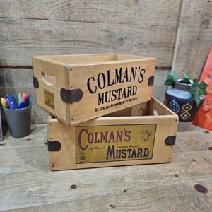 May include: Two wooden boxes with Colman's Mustard labels. The top box has the text "COLMAN'S MUSTARD BY SPECIAL APPOINTMENT TO THE KING". The bottom box has the text "COLMAN'S of Norwich Original English MUSTARD KING".