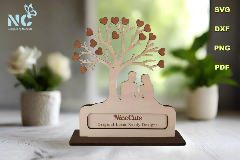 Puede incluir: Un recorte de madera de un &aacute;rbol con corazones en las ramas y una pareja de pie debajo. El &aacute;rbol est&aacute; sobre una base con el texto "NiceCuts Original Laser Ready Designs".